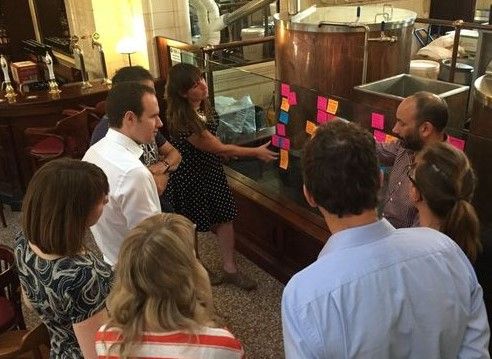 Small group of people stood round a glass wall covered in post-its. 