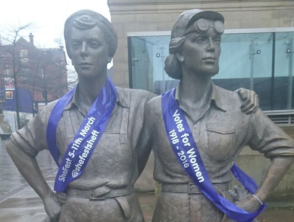 Photo of the women of steel statue in Sheffield wrapped in purple banners saying SheFest Votes for Women 